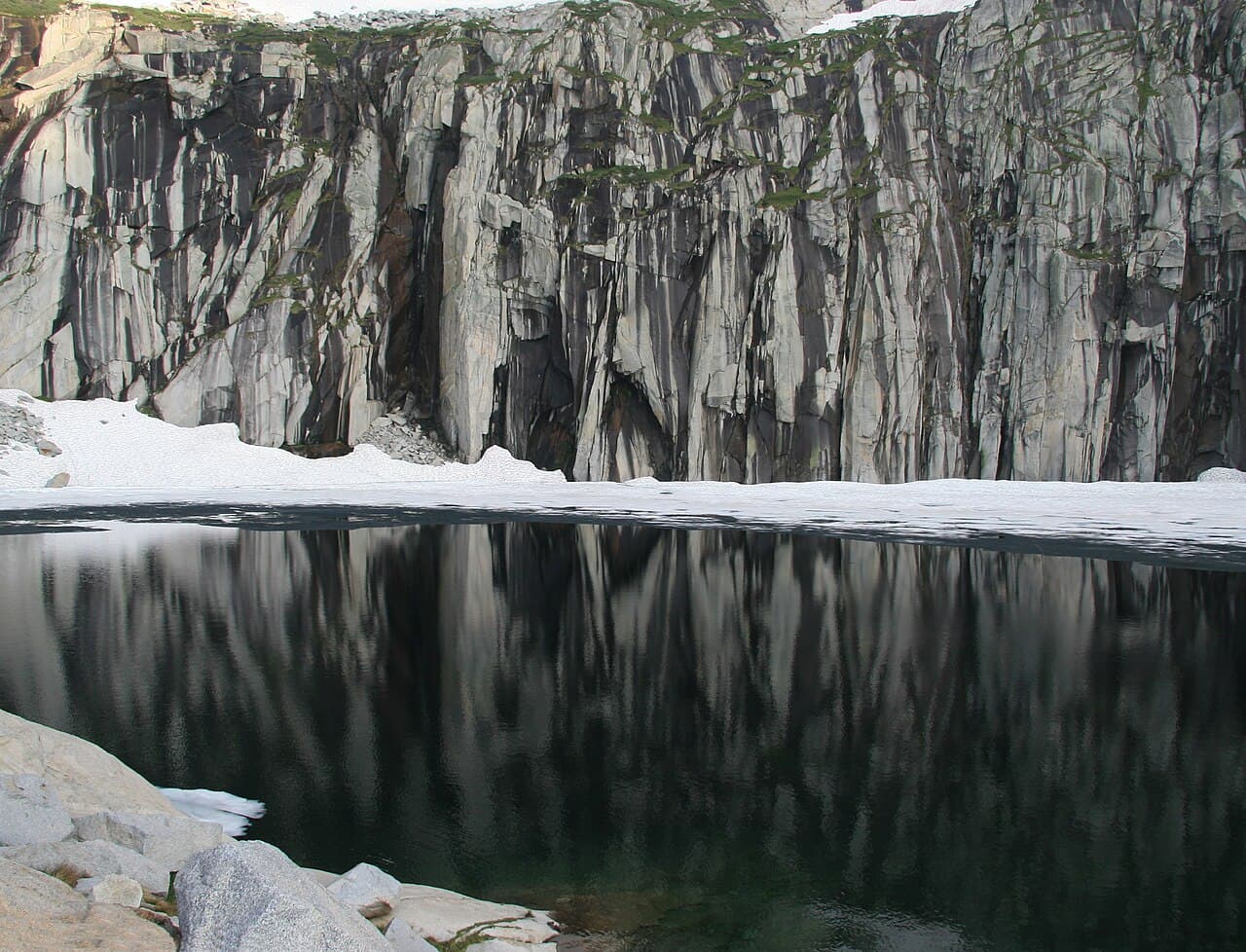 Dark granite wall and snow reflected in Precipice Lake